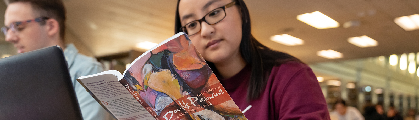 a sociology student reads a textbook in the library